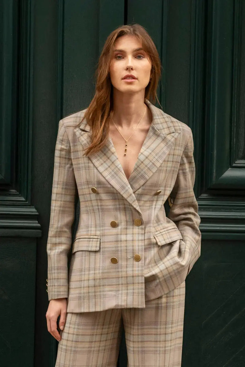 Cette veste tailleur croisée à carreaux gris bleu a une coupe longue et structurée. Elle présente un large col et des poches passepoils à rabat et la fente au milieu du dos. Entièrement doublée, elle se distingue par ses boutons en vieux or texturé sur le devant et aux manches.
