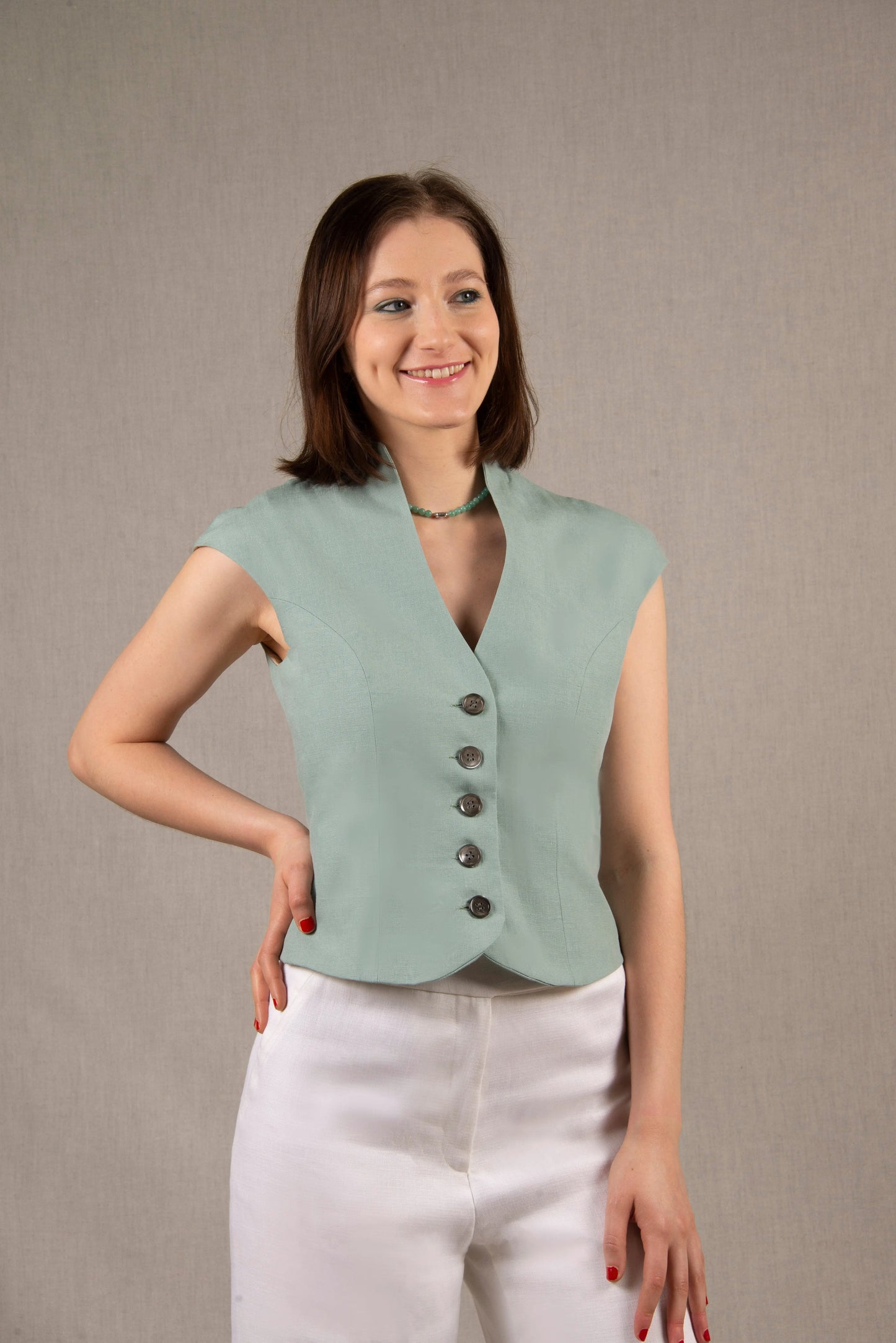Ce gilet a une coupe cintrée qui souligne la taille, avec des découpes princesse sur le devant et dans le dos. Les manches sont courtes et prolongent la ligne des épaules. L'encolure  est ouverte et profonde. Il y a cinq boutons en nacre sur le devant et le bas devant est légèrement arrondi. 