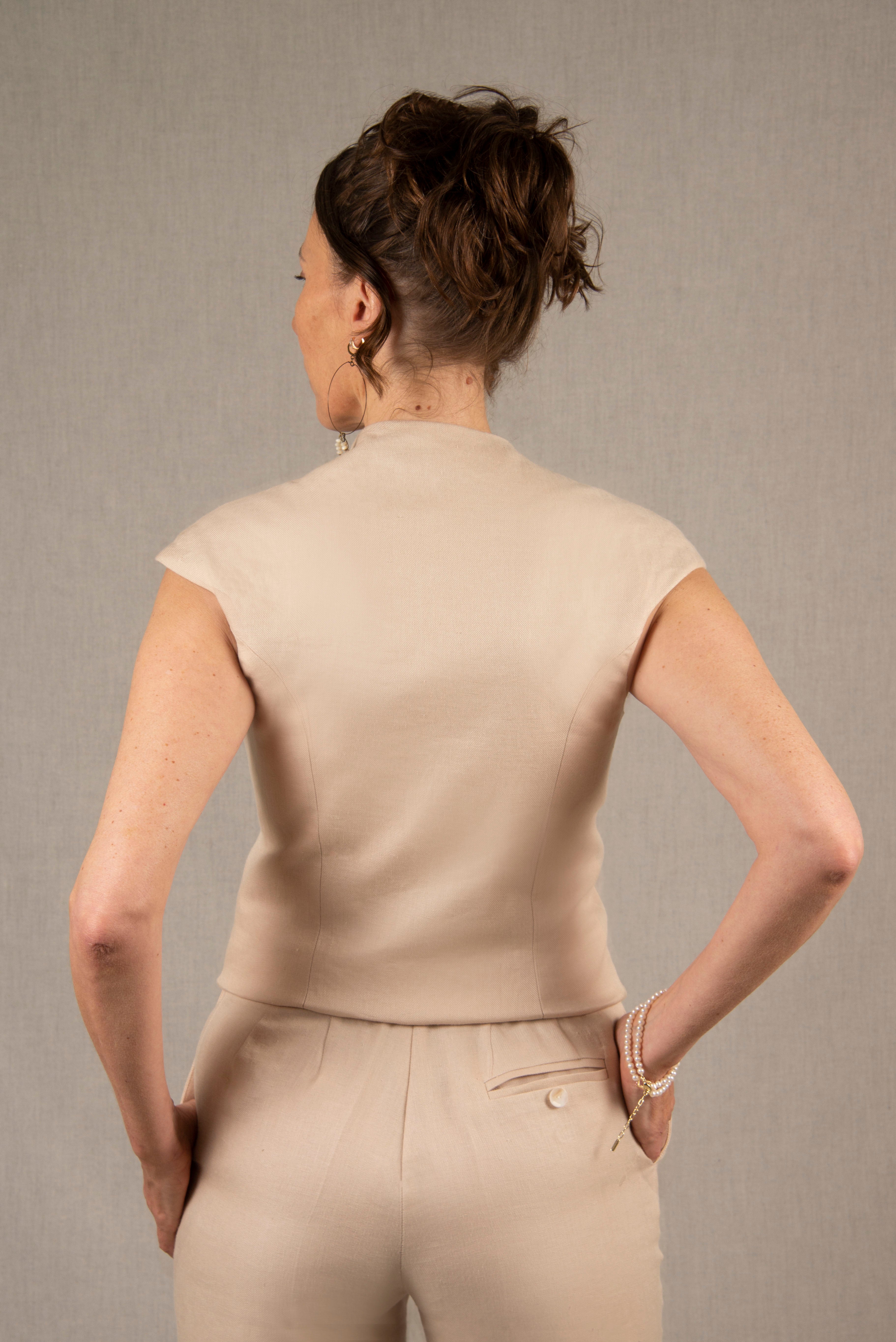 Ce gilet a une coupe cintrée qui souligne la taille, avec des découpes princesse sur le devant et dans le dos. Les manches sont courtes et prolongent la ligne des épaules. L'encolure  est ouverte et profonde. Il y a cinq boutons en nacre sur le devant et le bas devant est légèrement arrondi. 