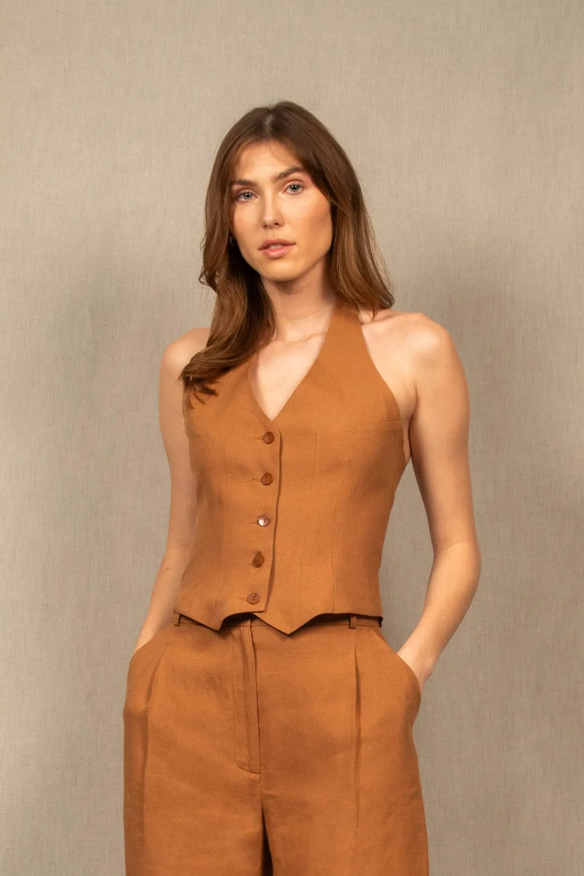Ce gilet dos nu est en 100% lin, couleur cognac. De nombreuses pinces cintrent le top et galbent le buste.
Il se ferme par une série de 5 boutons mates ton sur ton et sa hauteur se règle grâce à un jeu de coulisse dans le cou.