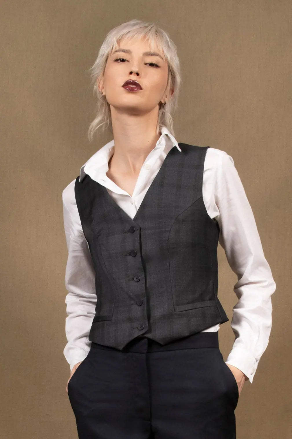 Gilet tailleur femme en 100% laine, couleur bleu marine.  Cinq boutons en nacre mates ton sur ton sur le devant, ainsi que deux poches passepoilées. La coupe de ce gilet est cintrée. La doublure est en 100% viscose avec un coloris ambré.