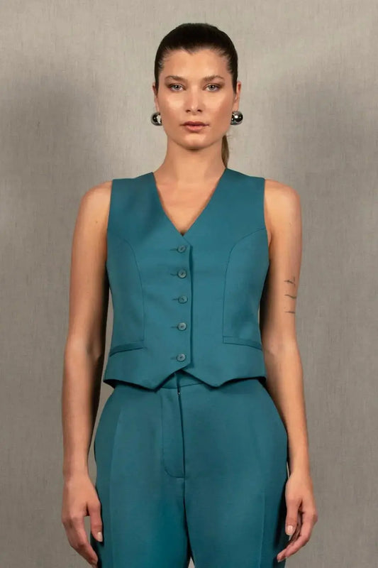 Gilet tailleur femme en 100% laine, couleur bleu pacifique.  Cinq boutons en nacre mates ton sur ton sur le devant, ainsi que deux poches passepoilées. La coupe de ce gilet est cintrée. La doublure est en 100% viscose avec un coloris ambré.