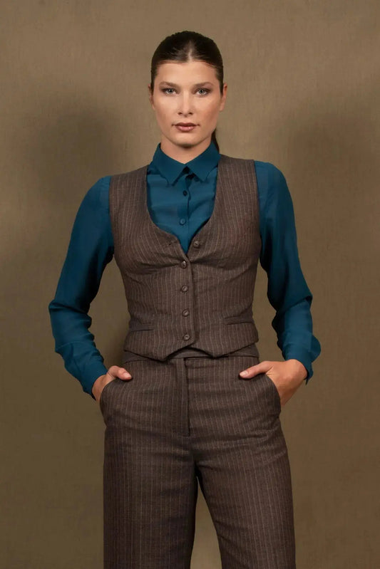 Gilet tailleur femme en 100% laine, couleur marron rayé. Cinq boutons en nacre mates ton sur ton sur le devant, ainsi que deux poches passepoilées. La coupe de ce gilet est cintrée. La doublure est en 100% viscose avec un coloris ambré.