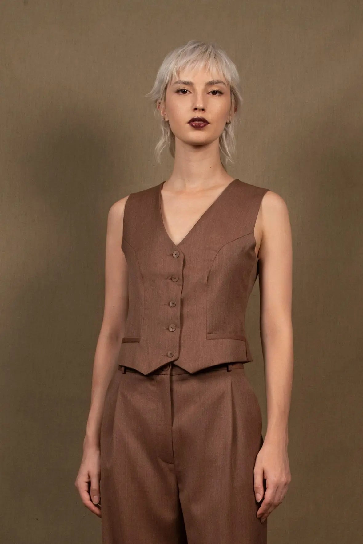 Gilet tailleur femme en 100% laine, couleur tomette.  Cinq boutons en nacre mates ton sur ton sur le devant, ainsi que deux poches passepoilées. La coupe de ce gilet est cintrée. La doublure est en 100% viscose avec un coloris ambré.