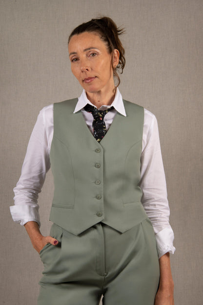 Gilet tailleur femme en 100% laine, couleur vert sauge.  Cinq boutons en nacre mates ton sur ton sur le devant, ainsi que deux poches passepoilées. La coupe de ce gilet est cintrée. La doublure est en 100% viscose avec un coloris ambré.