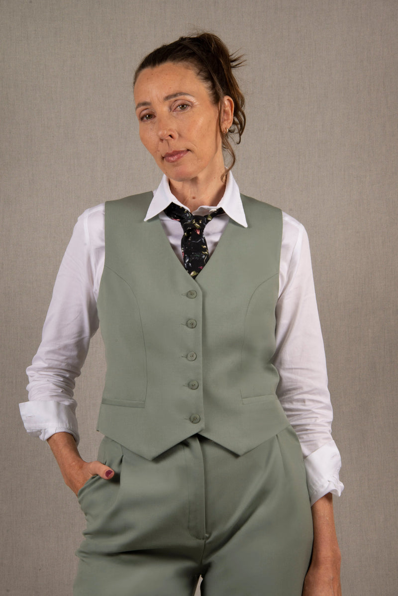 Gilet tailleur femme en 100% laine, couleur vert sauge.  Cinq boutons en nacre mates ton sur ton sur le devant, ainsi que deux poches passepoilées. La coupe de ce gilet est cintrée. La doublure est en 100% viscose avec un coloris ambré.