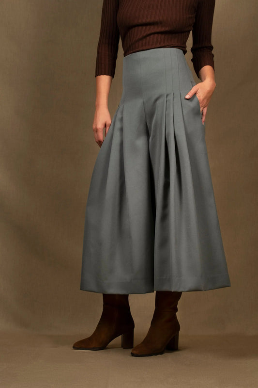 Ce pantalon femme se distingue par une élégante silhouette évasée. Pantalon taille haute ponctué par de larges plis sur le devant, ce modèle cintré à la taille flatte votre silhouette. Il comporte deux poches dans la couture, sur chaque côtés. Une fermeture éclair invisible se situe à l’arrière. Longueur au dessus de la cheville.