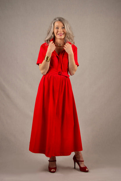 Cette robe chemisier 100% coton, à longueur sous-mollet, a un boutonnage caché sur tout le milieu devant. Elle a des manches courtes raglan avec une série de plis à la base, ainsi que deux poches plaquées à rabat sur la poitrine et deux poches sur les côtés dans la couture. Il y a un smock au milieu du dos pour cintrer la taille et une ceinture large surpiquée finie par une boucle en métal.
