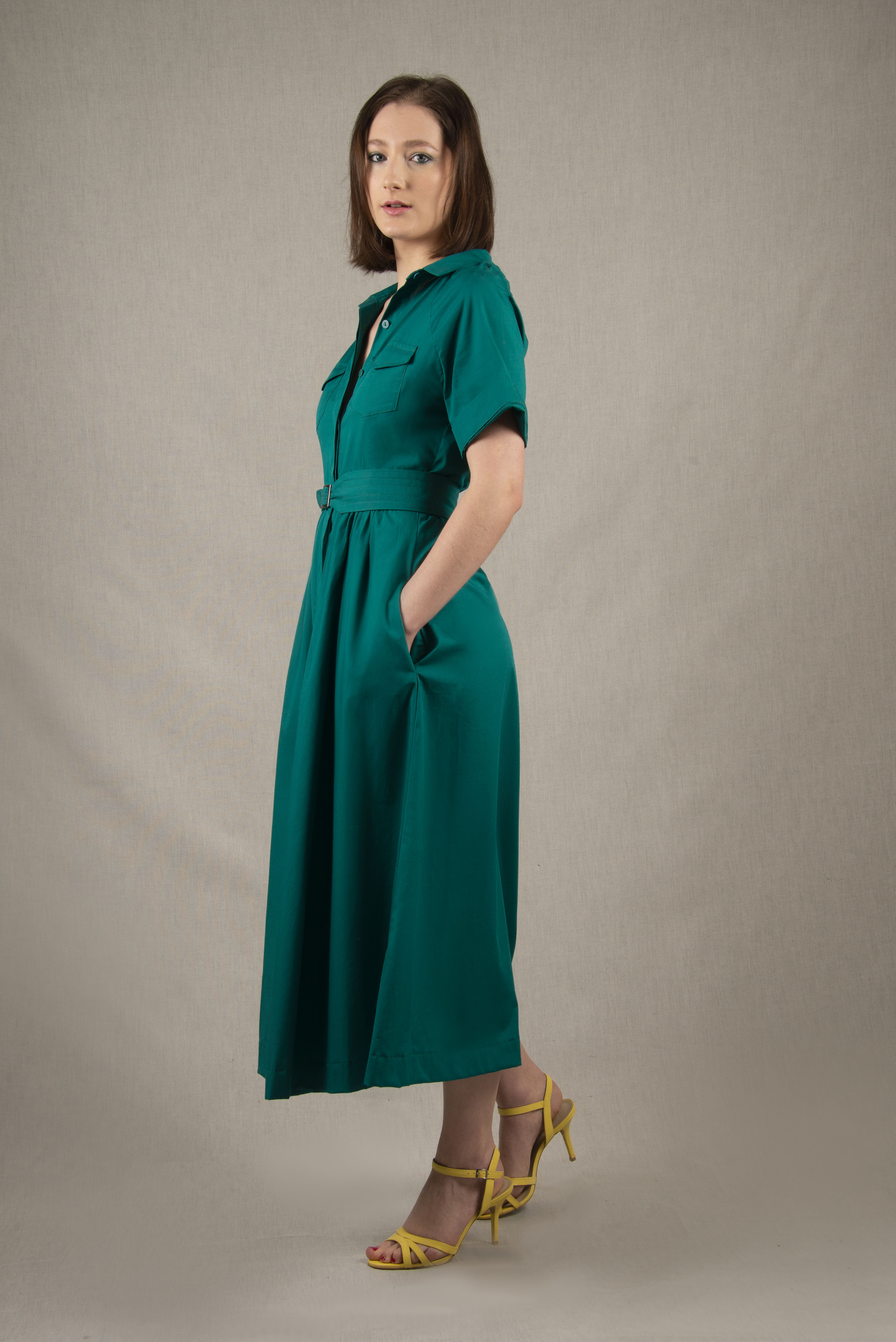 Cette robe chemisier 100% coton, à longueur sous-mollet, a un boutonnage caché sur tout le milieu devant. Elle a des manches courtes raglan avec une série de plis à la base, ainsi que deux poches plaquées à rabat sur la poitrine et deux poches sur les côtés dans la couture. Il y a un smock au milieu du dos pour cintrer la taille et une ceinture large surpiquée finie par une boucle en métal.