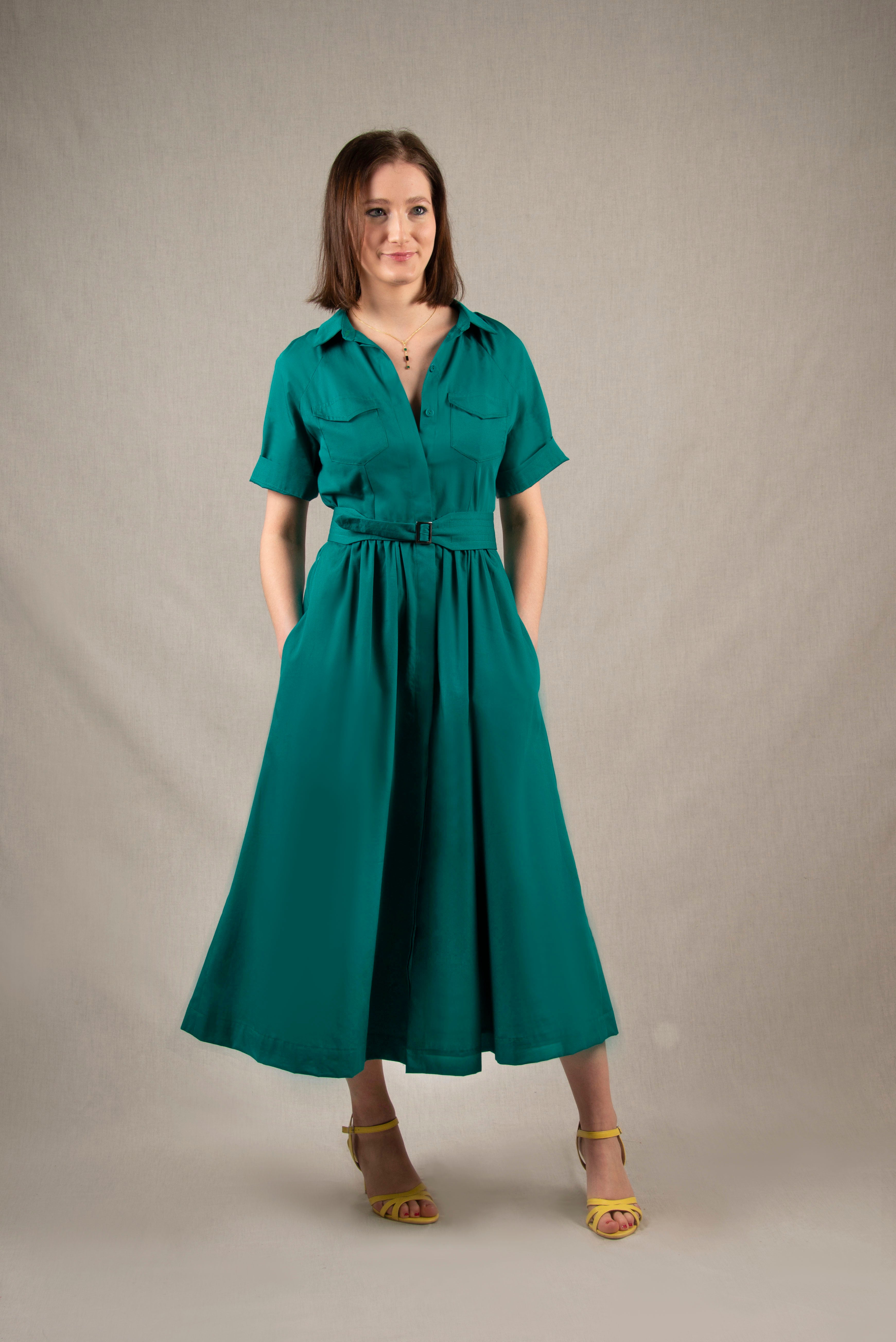 Cette robe chemisier 100% coton, à longueur sous-mollet, a un boutonnage caché sur tout le milieu devant. Elle a des manches courtes raglan avec une série de plis à la base, ainsi que deux poches plaquées à rabat sur la poitrine et deux poches sur les côtés dans la couture. Il y a un smock au milieu du dos pour cintrer la taille et une ceinture large surpiquée finie par une boucle en métal.