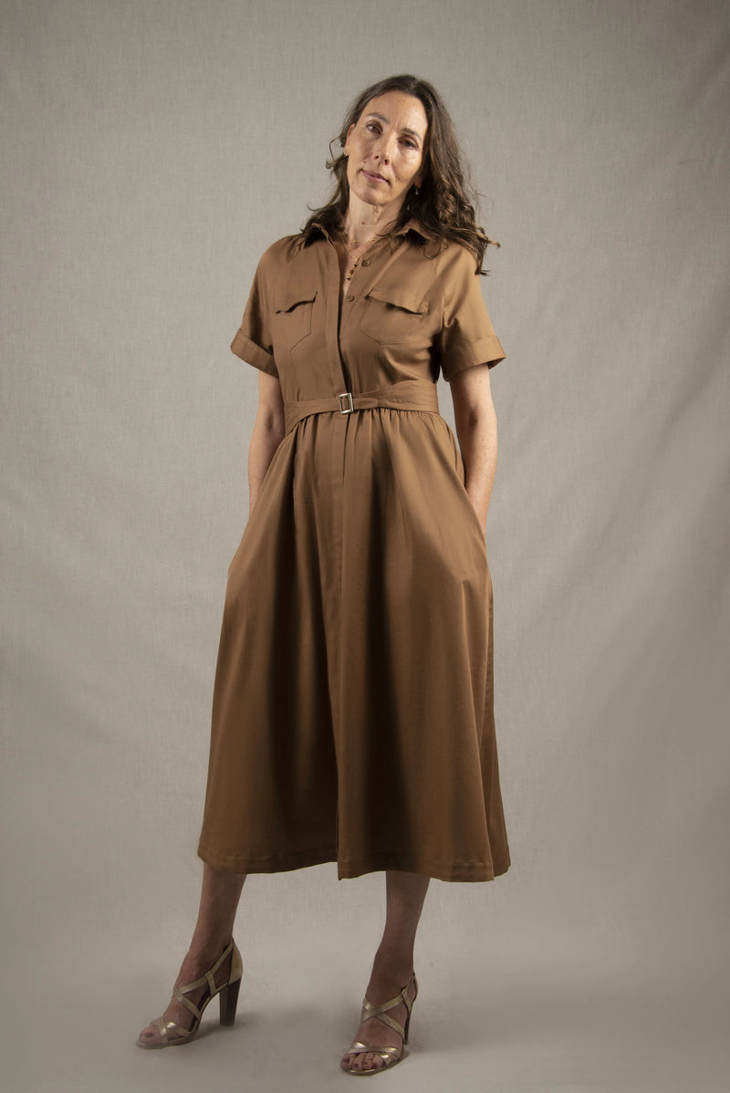 Cette robe chemisier 100% coton, à longueur sous-mollet, a un boutonnage caché sur tout le milieu devant. Elle a des manches courtes raglan avec une série de plis à la base, ainsi que deux poches plaquées à rabat sur la poitrine et deux poches sur les côtés dans la couture. Il y a un smock au milieu du dos pour cintrer la taille et une ceinture large surpiquée finie par une boucle en métal.