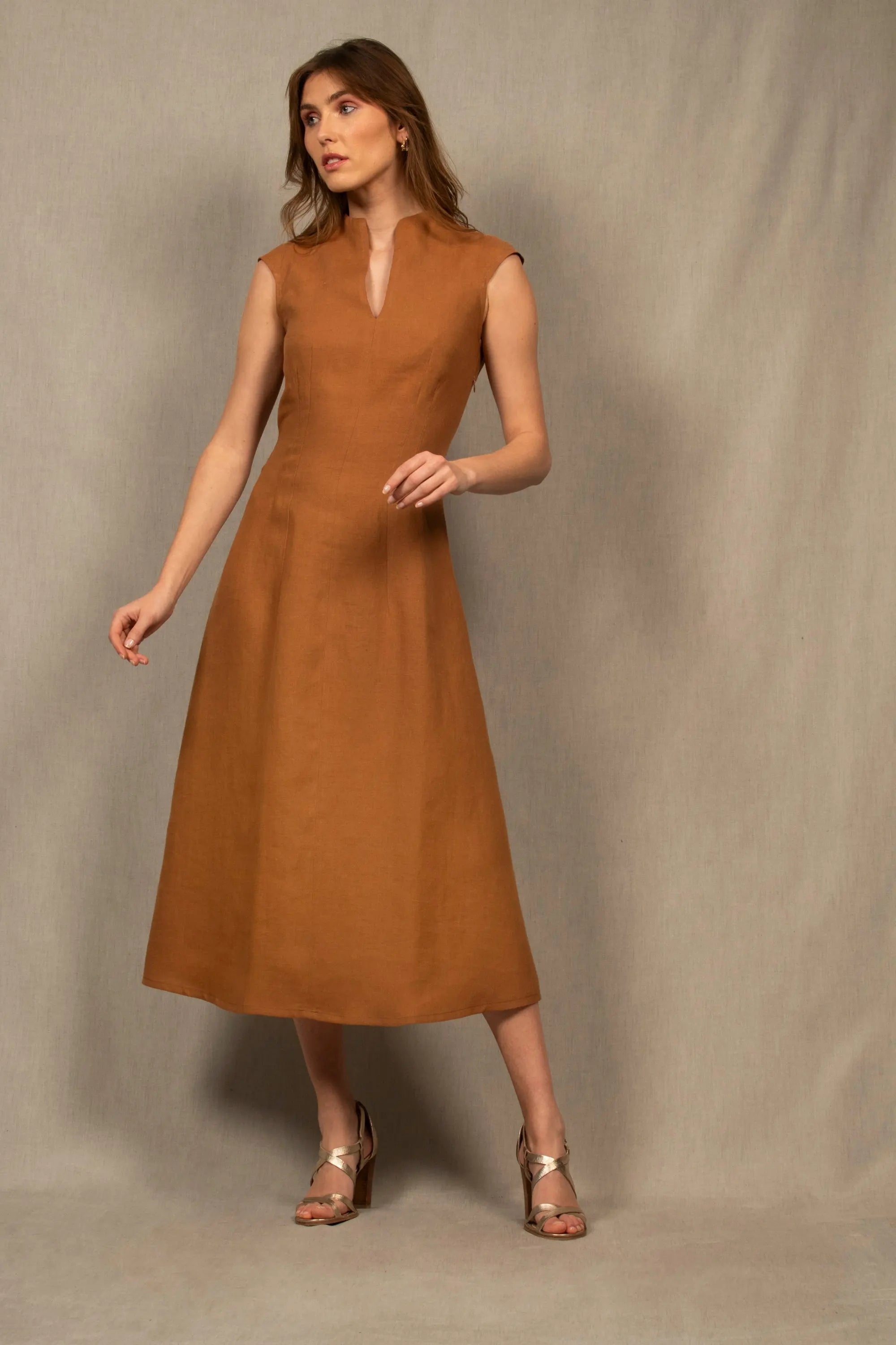 Robe en lin, couleur cognac,  légèrement évasée longueur à la cheville. La taille est marquée par un jeu de pinces. Il y a un ouverture dans le bas du dos au niveau de la taille. Fermeture par zip invisible côté gauche. Col légèrement montant avec fente milieu devant.