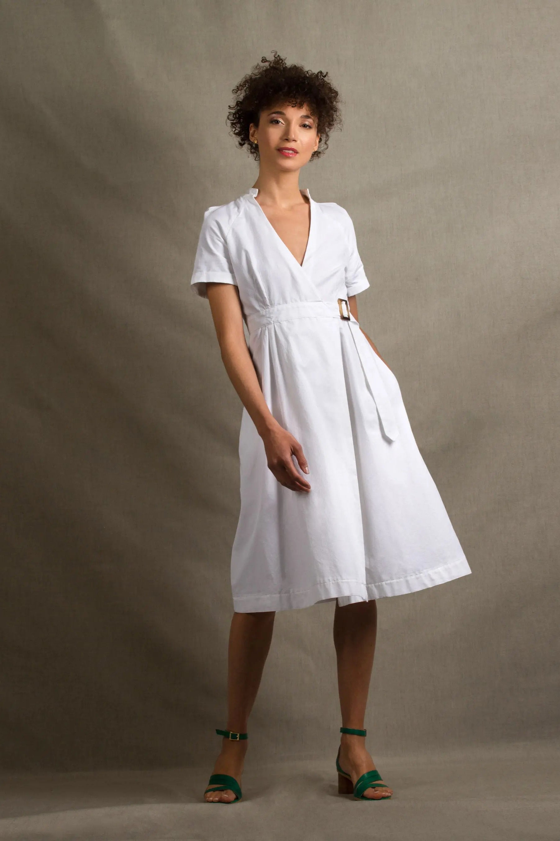 Cette robe en coton blanc a une coupe portefeuille, manches courtes, col en V, fermeture par ceinture intégrée avec boucle effet corne.