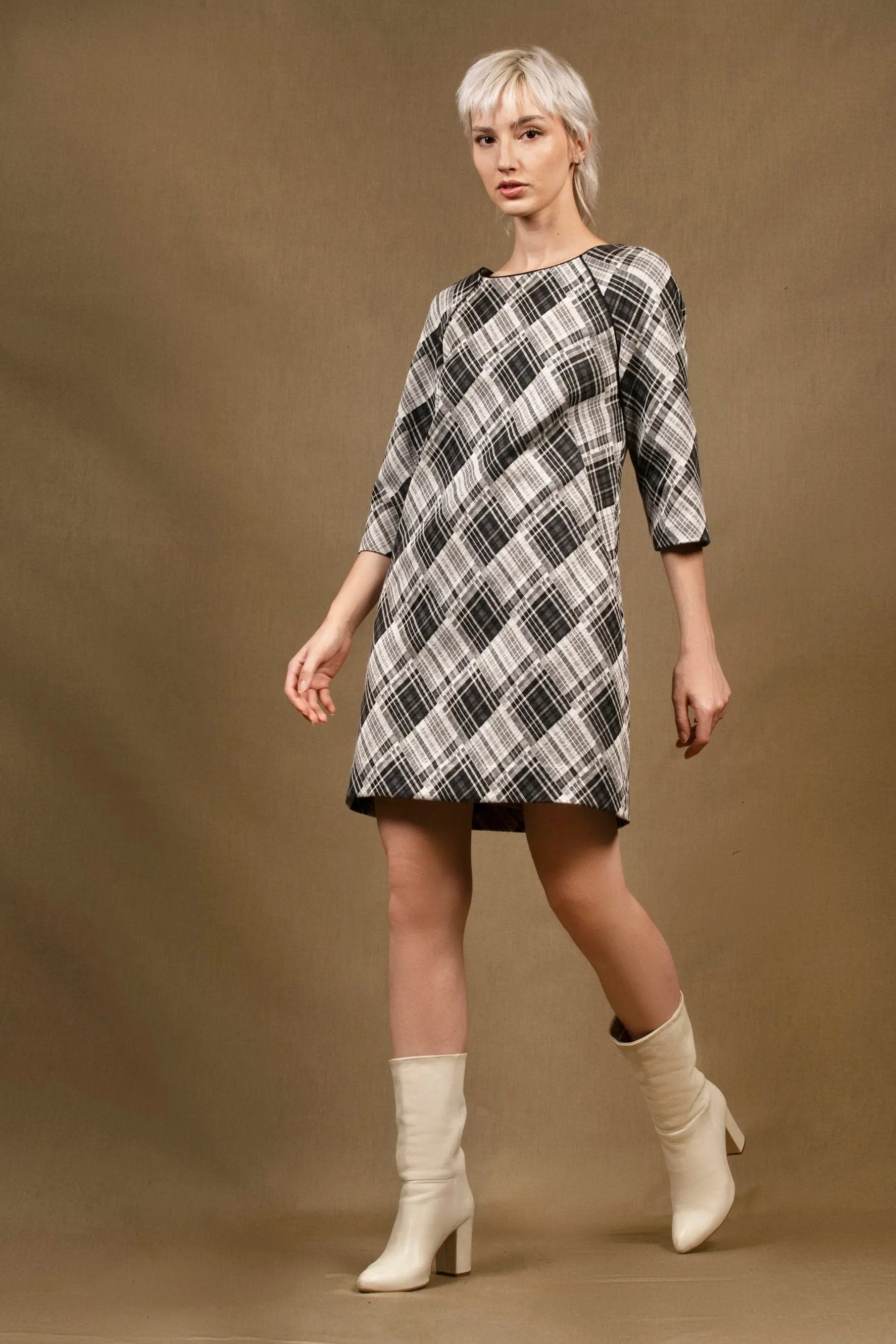 obe droite légèrement évasée, longueur au-dessus du genou et manches trois-quarts. Col bateau bordé d’un passepoil en soie noire. Une grande pince oblique galbe le devant et deux pinces dans le dos viennent subtilement marquer la taille. Elle se ferme par une fermeture sur le côté et est entièrement doublée. Coton et viscose à losanges noir et gris clair