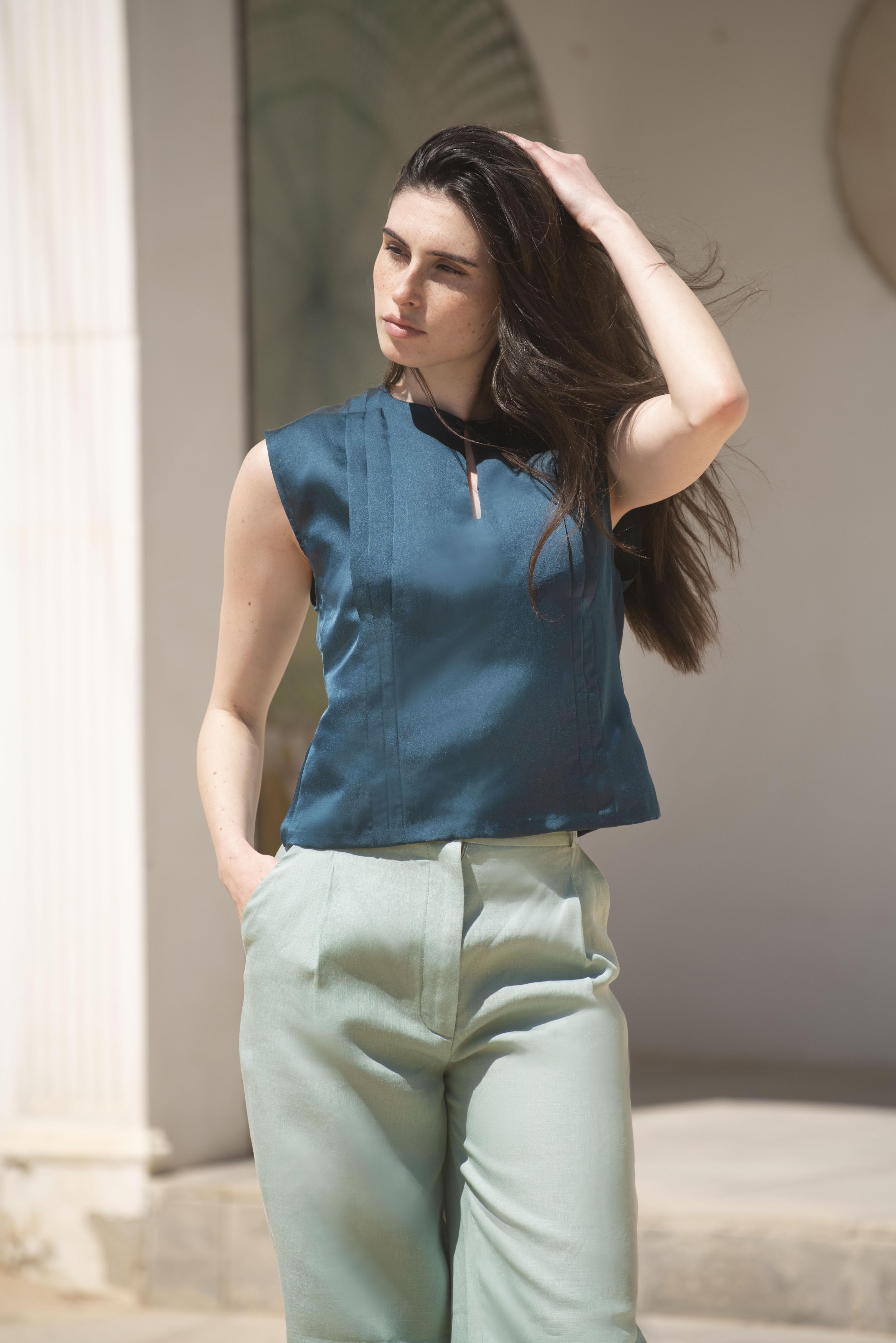 Top femme sans manches en soie bleu pétrole, coupe droite légèrement cintrée, encolure ronde dégagée avec bouton, dos ouvert partiellement fermé par bride et boutons, plis plats verticaux sur le devant et boutons ton sur ton en nacre.