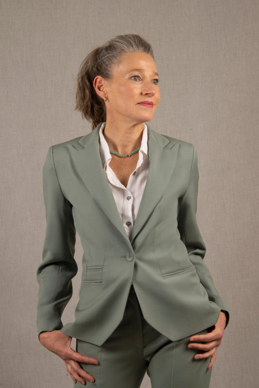 Veste tailleur femme vert sauge en laine, coupe cintrée, col tailleur cranté, boutonnage simple, trois poches passepoilées. Elle présente également une poche intérieure.