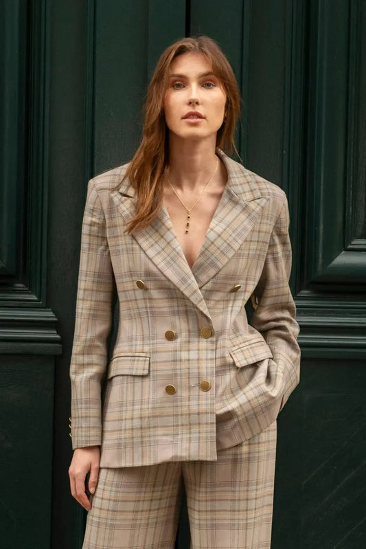 Cette veste tailleur croisée à carreaux gris bleu a une coupe longue et structurée. Elle présente un large col et des poches passepoils à rabat et la fente au milieu du dos. Entièrement doublée, elle se distingue par ses boutons en vieux or texturé sur le devant et aux manches. 
